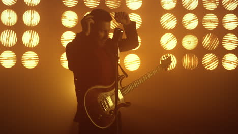 un guitarrista sexy cantando de pie en el escenario con luces de fondo. un tipo interpretando una canción.