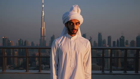 emirati businessman in traditional clothing posing on a rooftop in dubai at sunset, with the burj khalifa and city skyline highlighting success and cultural pride