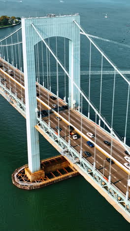 Cars going to and from the Bronx, New York. Aerial view of the Throgs Neck Bridge on sunny day. Boats sailing on the East River at backdrop. Vertical video
