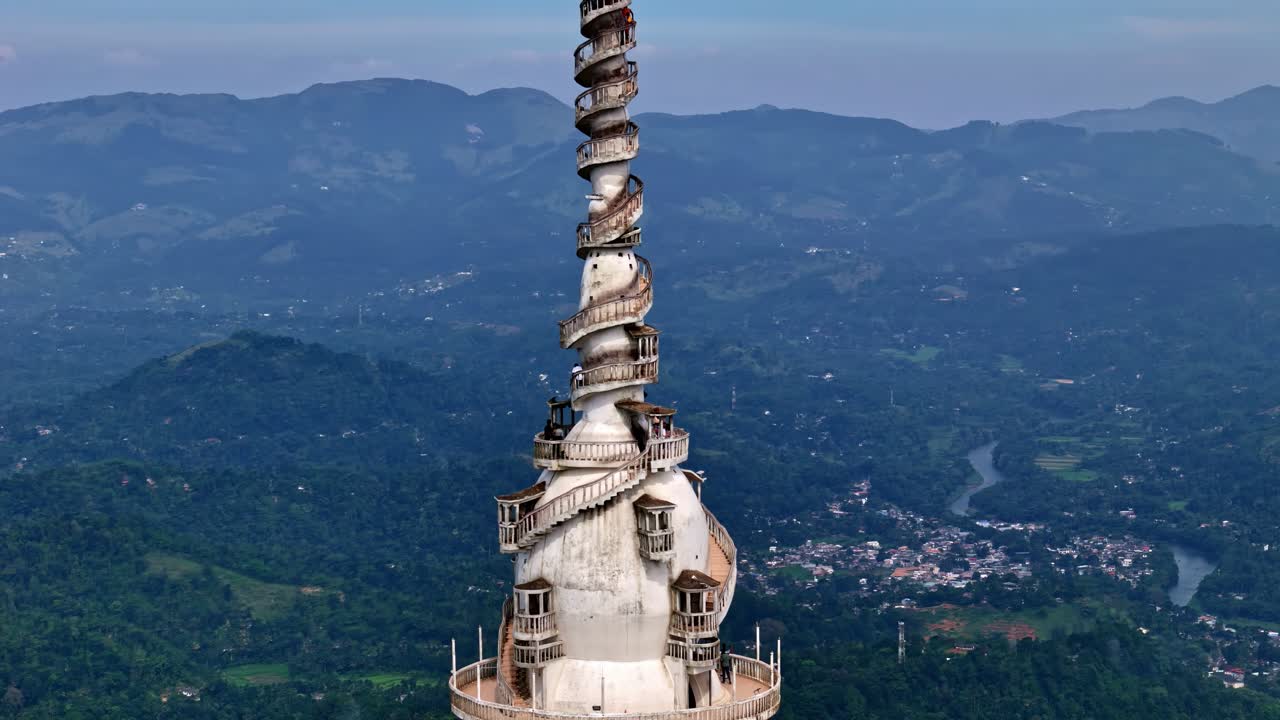 Close-up drone shot of the iconic white spiral Ambuluwawa tower spire rising high above green hills and distant blue mountains in Sri Lanka’s countryside