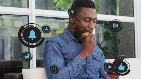 network of digital icons moving against african american man using smartphone while having a snack