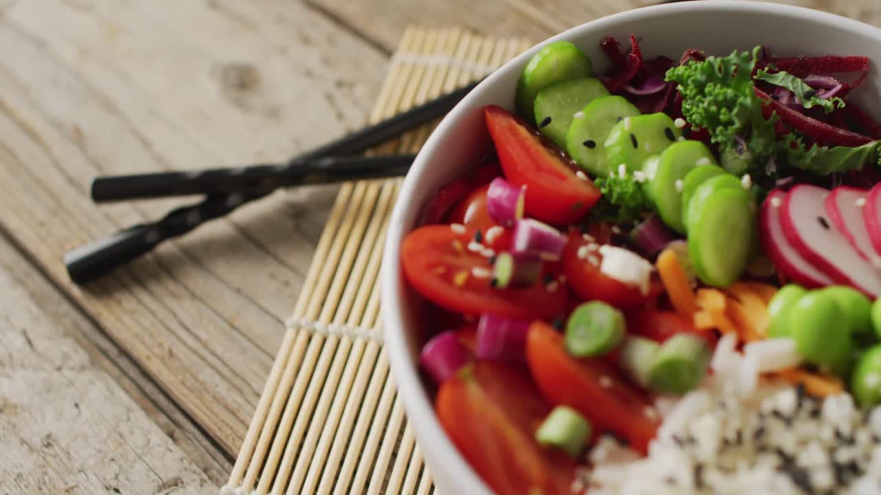 Composition of bowl of rice and vegetables with chopsticks on wooden background