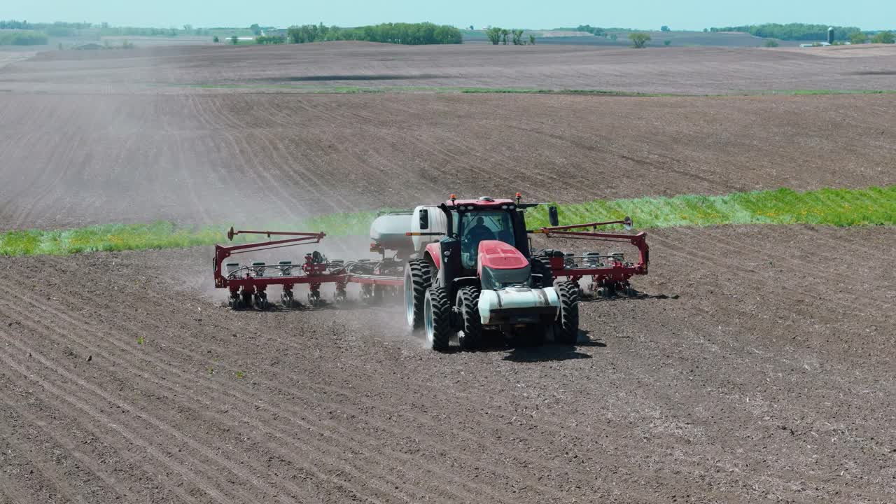 Drone footage of a farmer planting corn seeds in an iowa field in a red tractor