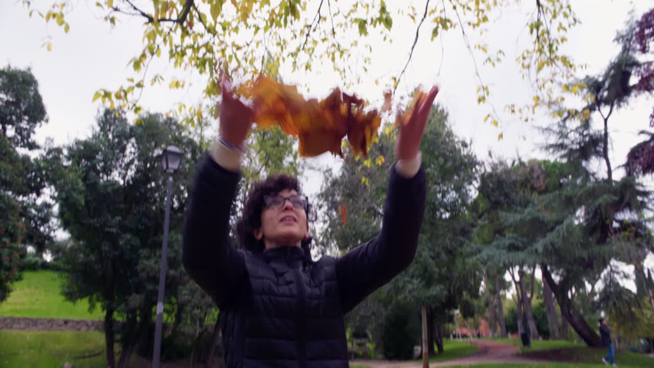 Donna felice lancia foglie autunnali in un parco
