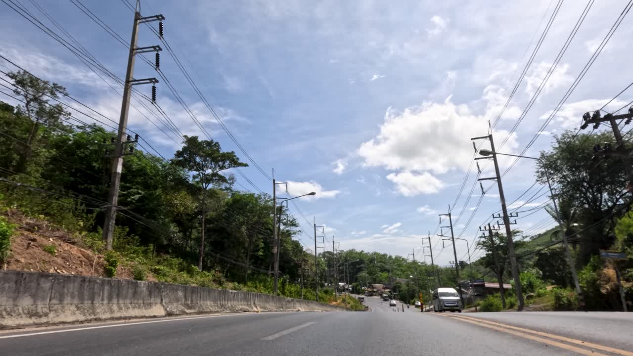 Low-angle moving shot of tropical street with traffic, power lines, and lush greenery under sunlight