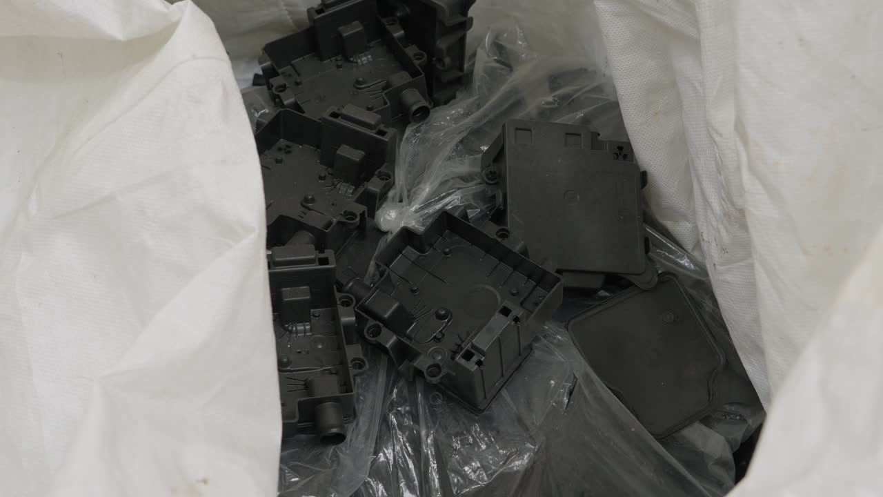 Kasserte svarte plastkapslinger og komponentdeksler i en hvit innsamlingspose