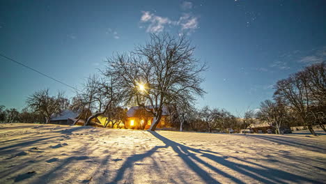 Timelapse-of-sunrays-filtering-through-tree-branches-with-illuminated-house-in-background-in-snowy-landscape