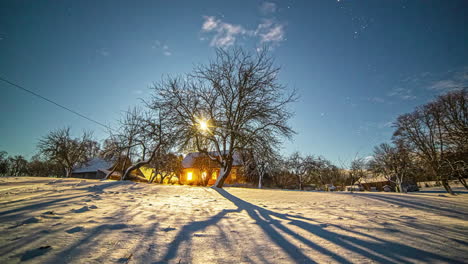 timelapse of sunrays filtering through tree branches with illuminated house in background in snowy landscape