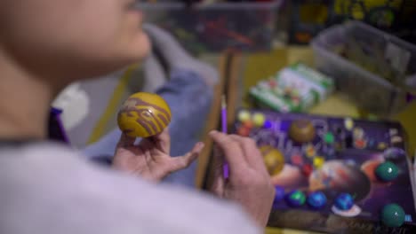 back view, over the shoulder footage of caucasian woman, painting a toy planet, creating solar system