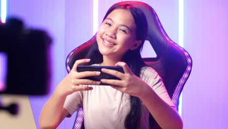 excited asian kid girl playing video game with mobile phone then smiles to camera while live stream