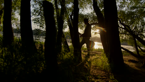 person walking through a forest near a river at sunset