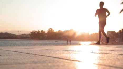 slow motion, silhouette of man jogging on pavement by ocean during golden hour
