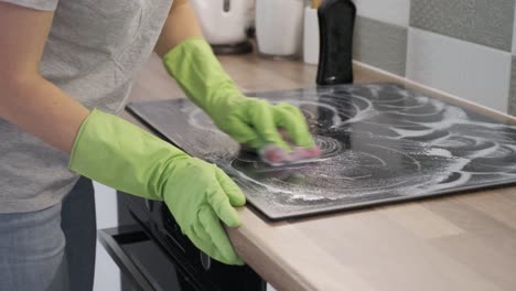 primer plano de la mano de la mujer limpiando la superficie eléctrica de la cerámica de vidrio de cocina moderna con esponja y detergente