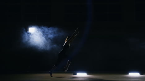 talented girl gymnast performs a flip turn in a jump on the gymnastics carpet in slow motion in a contoured light in the smoke. steadycam. rotation in the air