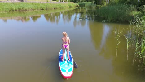 Volando-Por-Encima-De-Una-Joven-De-Pie-Remando-En-Una-Tabla-De-SUP-En-Un-Estanque-En-Verano