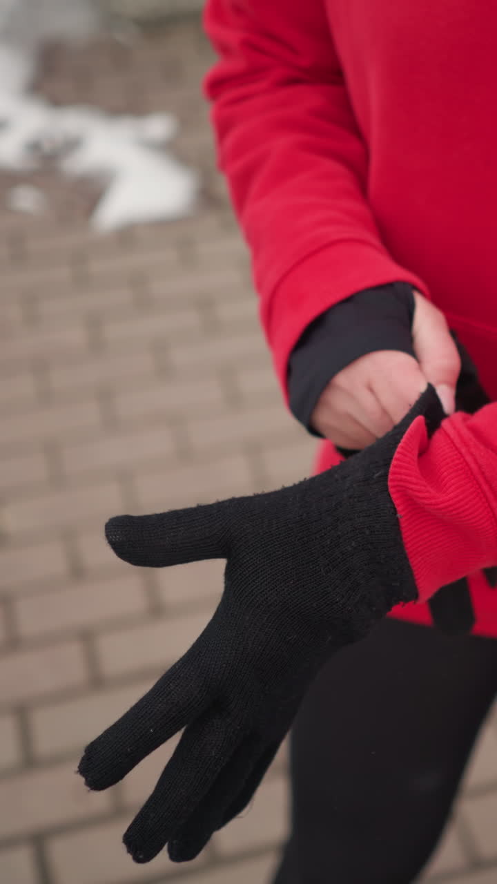 은 후디를 입은 여성이 을 따라 눈이 쌓인 길에 서서, 야외 도시 환경에서 추운 날씨에 따뜻함을 위해 검은 겨울 장갑을 착용하는 부분적 인 시각