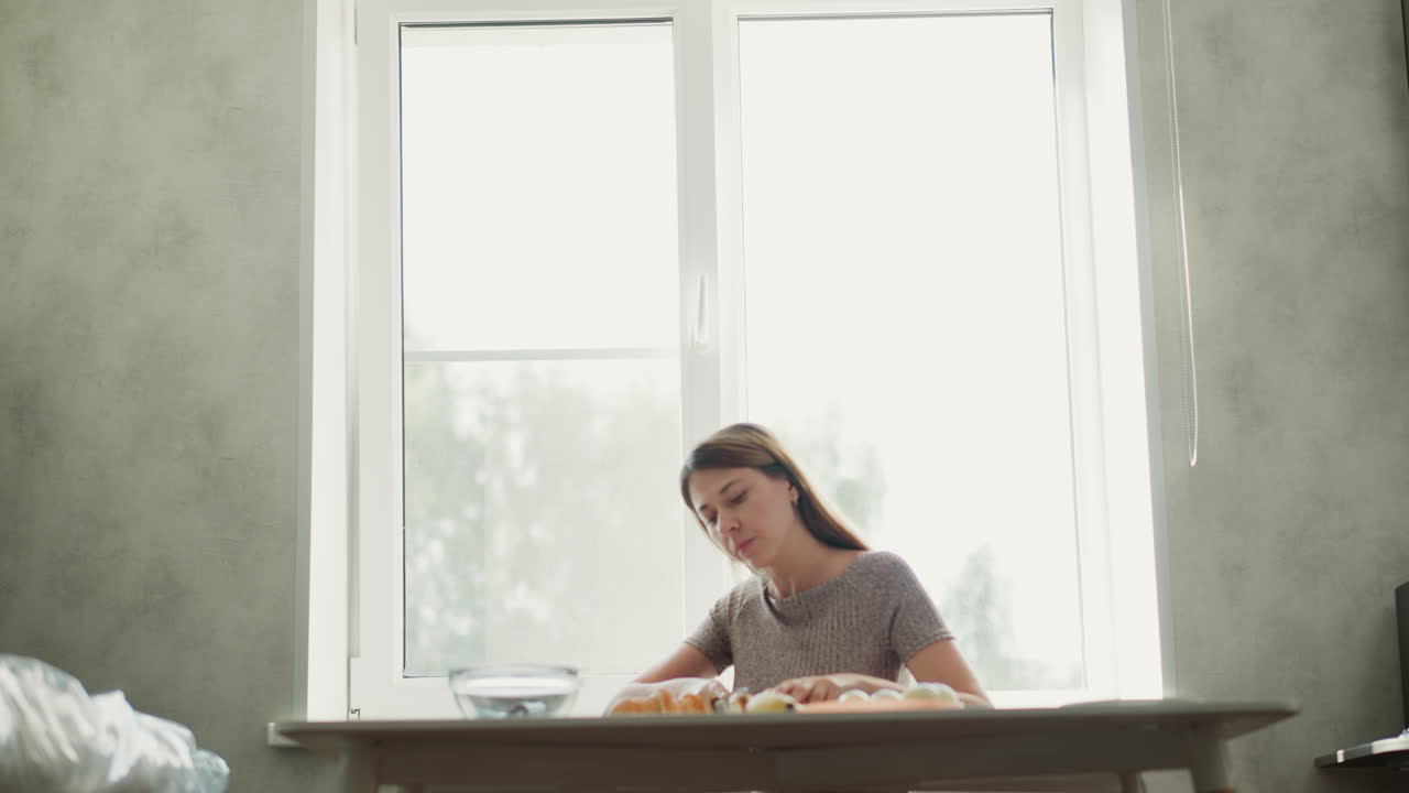 Woman preparing food at a kitchen table near a window