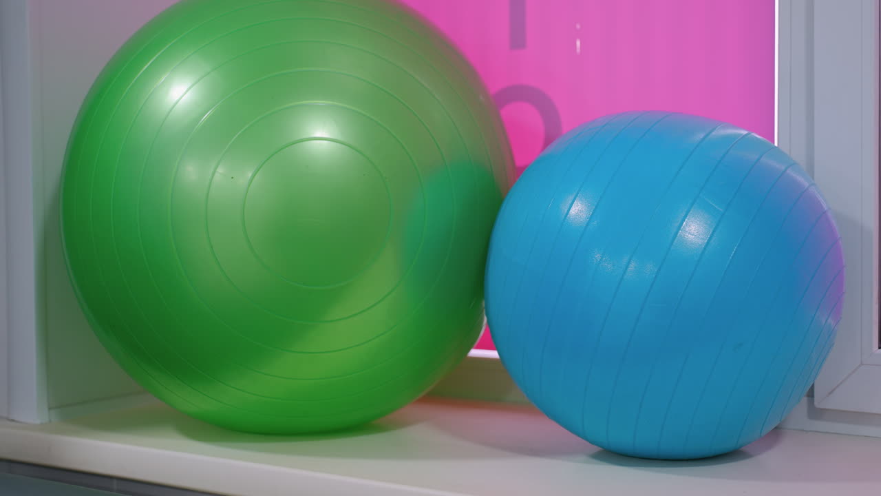 두 개의 안정 공, 하나는 녹색, 하나는 파란색, 활기찬 분홍색 배경으로 색 표면에 에 배치, 이 피트니스 공은 핵심 강화 및 스트레칭 운동에 필수적입니다.