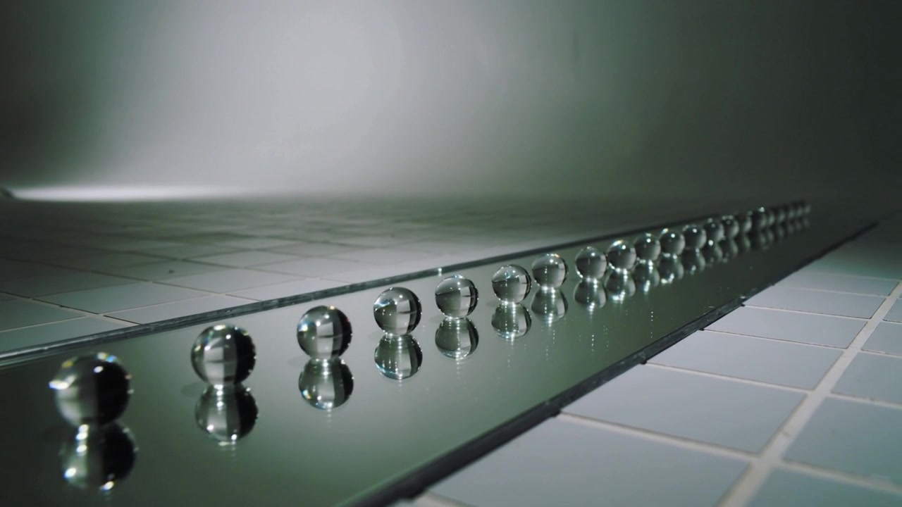 Moving low-angle camera revealing receding row of reflective metal spheres on mirrored rail