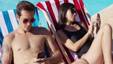 Young-couple-using-phones-at-the-swimming-pool