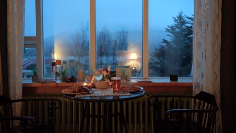 cozy evening dinner for two by window with mood lighting, pasta and drinks on table, overcast outdoor view