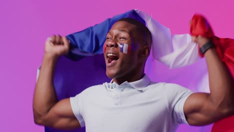 Happy-african-american-male-football-supporter-with-flag-of-france-over-pink-lighting