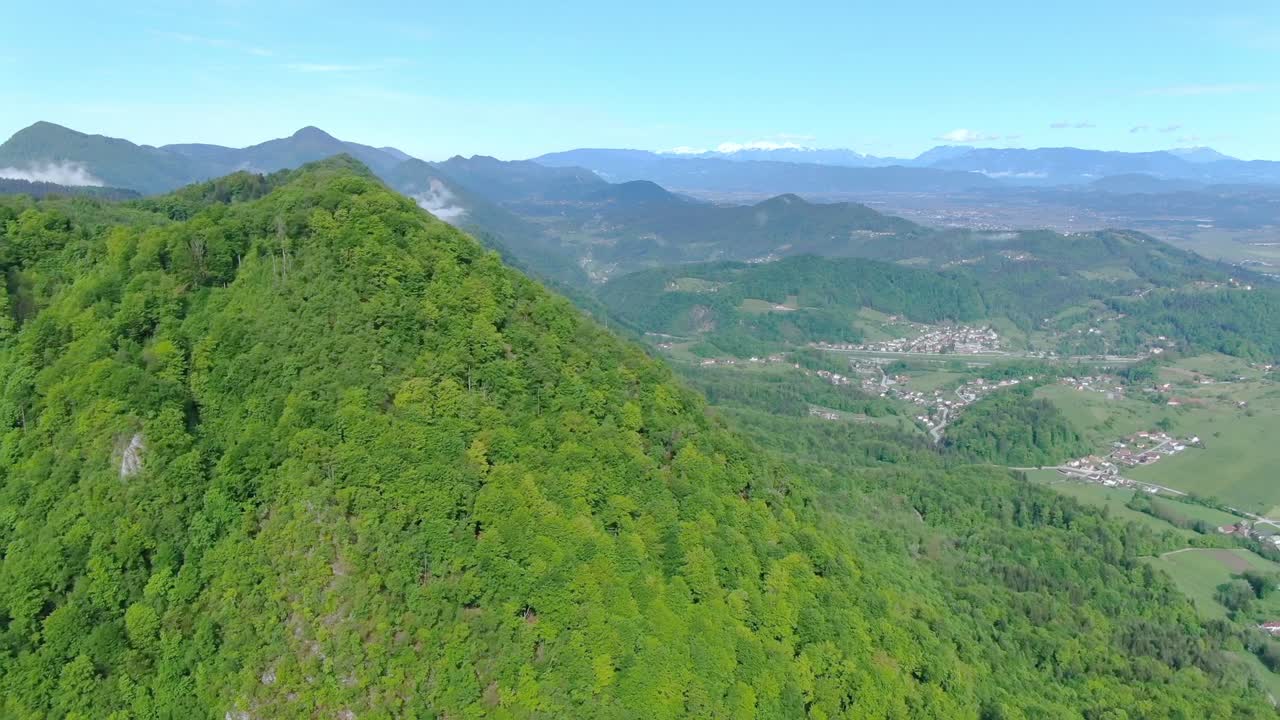 Green mountain range completely covered with trees. Village with houses and fields in valley at foot of mountain. Zoom out