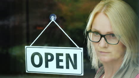 a portrait of a pensive salesman standing behind the glass door of the store at the plate open waiti