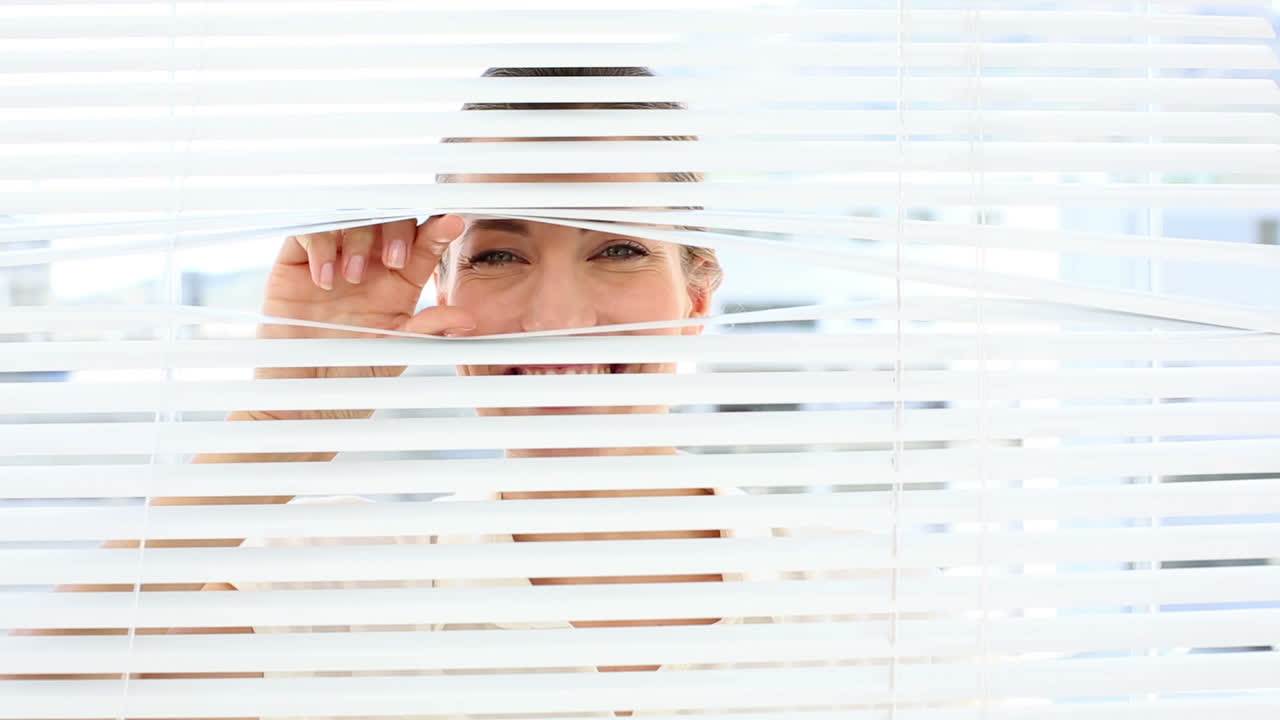 una mujer de negocios sonriente mirando a través de las persianas.