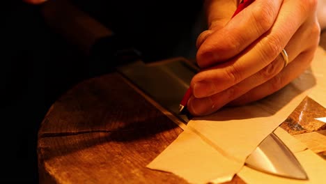 close-up of hands using a knife to cut paper on a wooden surface.