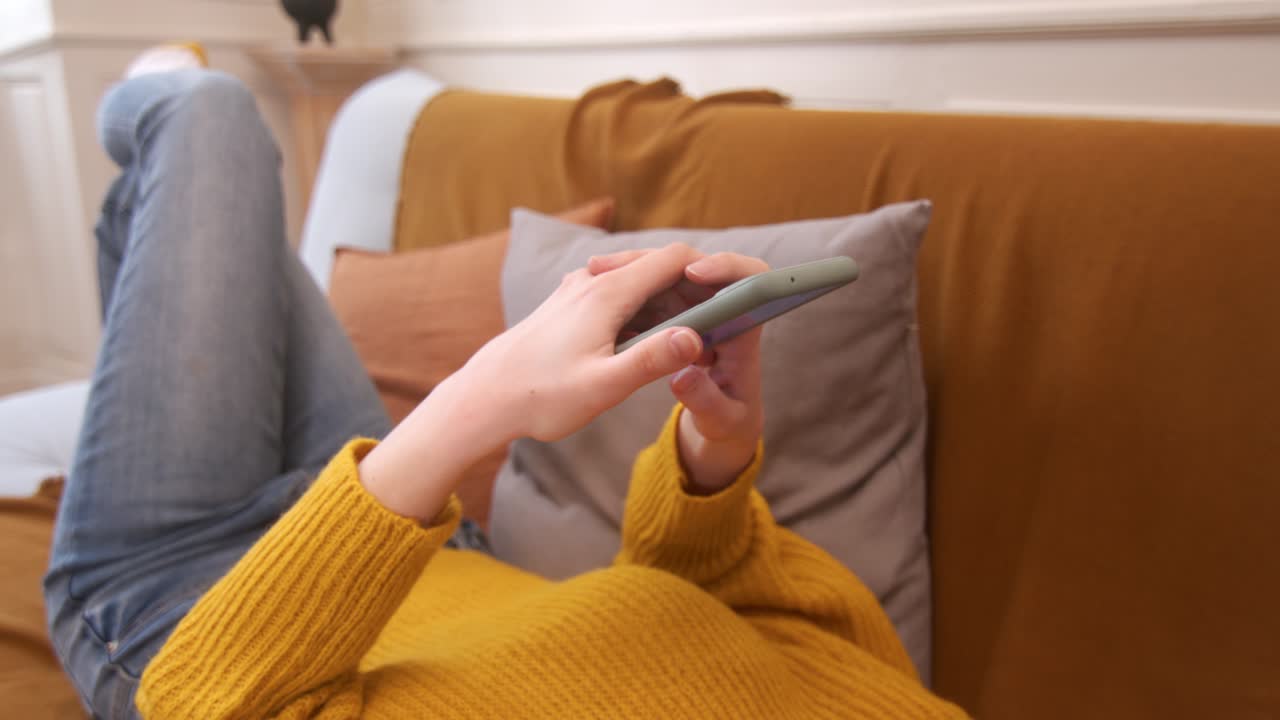 женщина лежит на диване, используя мобильный телефон дома.