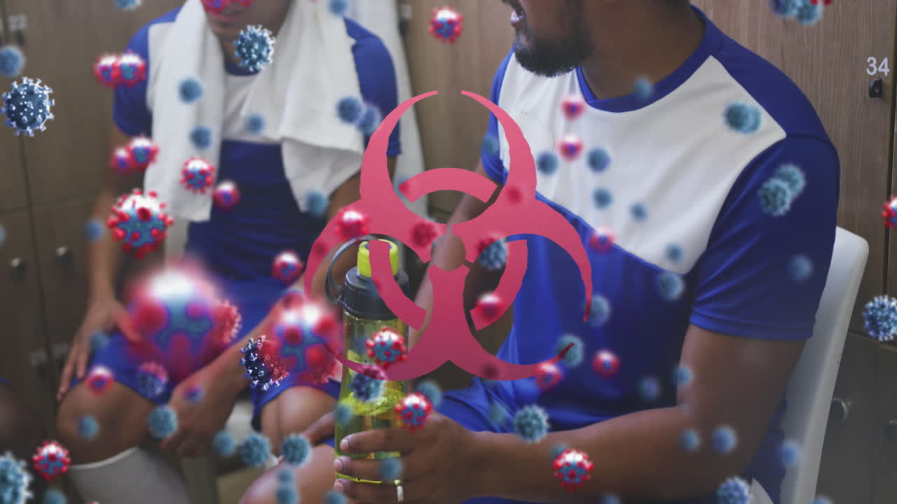 animación de células de virus y símbolo de riesgo biológico sobre un grupo de jugadores de fútbol en el vestuario