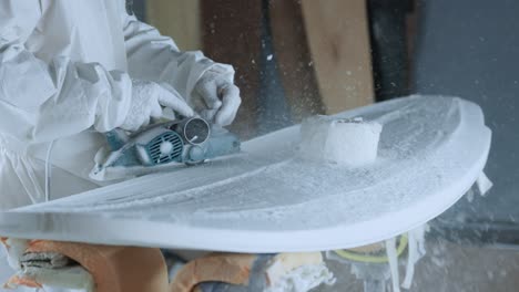 Cropped-anonymous-professional-master-polishing-surfboard-in-workshop