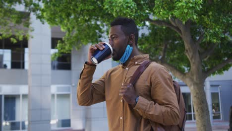 Afroamerikanischer-Geschäftsmann-Mit-Gesichtsmaske,-Der-Kaffee-In-Der-Stadtstraße-Trinkt