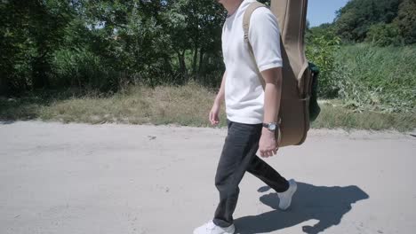 young man walking with guitar on street near forest