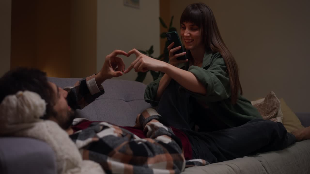 Couple relaxing on the couch, making heart shape with hands