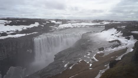 Majestic-waterfall-cascading-over-a-cliff-in-Iceland,-surrounded-by-snow-and-unique-land-patterns