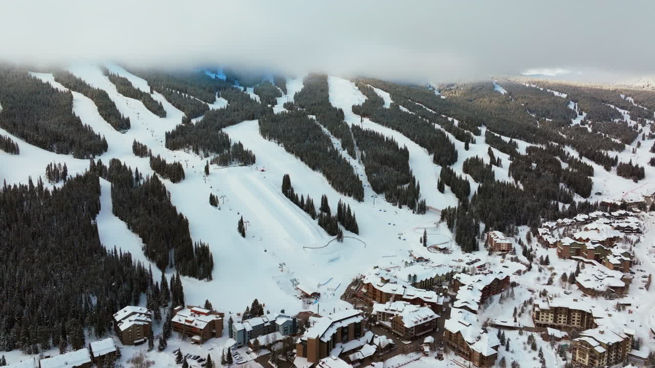 Sumu hälvenee pilvikerroksesta talvisena lumisena varhaisen aamun auringonnousun aikaan, ilmakuva dronella Copper Mountain Coloradon hiihtokeskuksesta, jossa näkyy i70 Eagle Flyer -hissi, keskuskylä, lumilautailun half pipe ja Ikon Epic -passin pysäköintialue eteenpäin