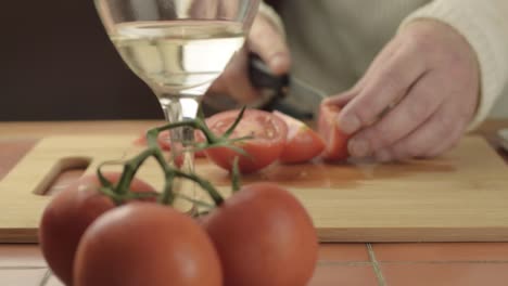 hands cutting fresh vine tomatoes in kitchen with glass of white wine medium shot