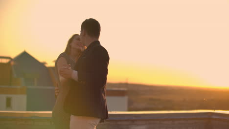 dos amantes abrazándose bailando en la parte superior de un rascacielos con vistas a la ciudad al amanecer y al atardecer.