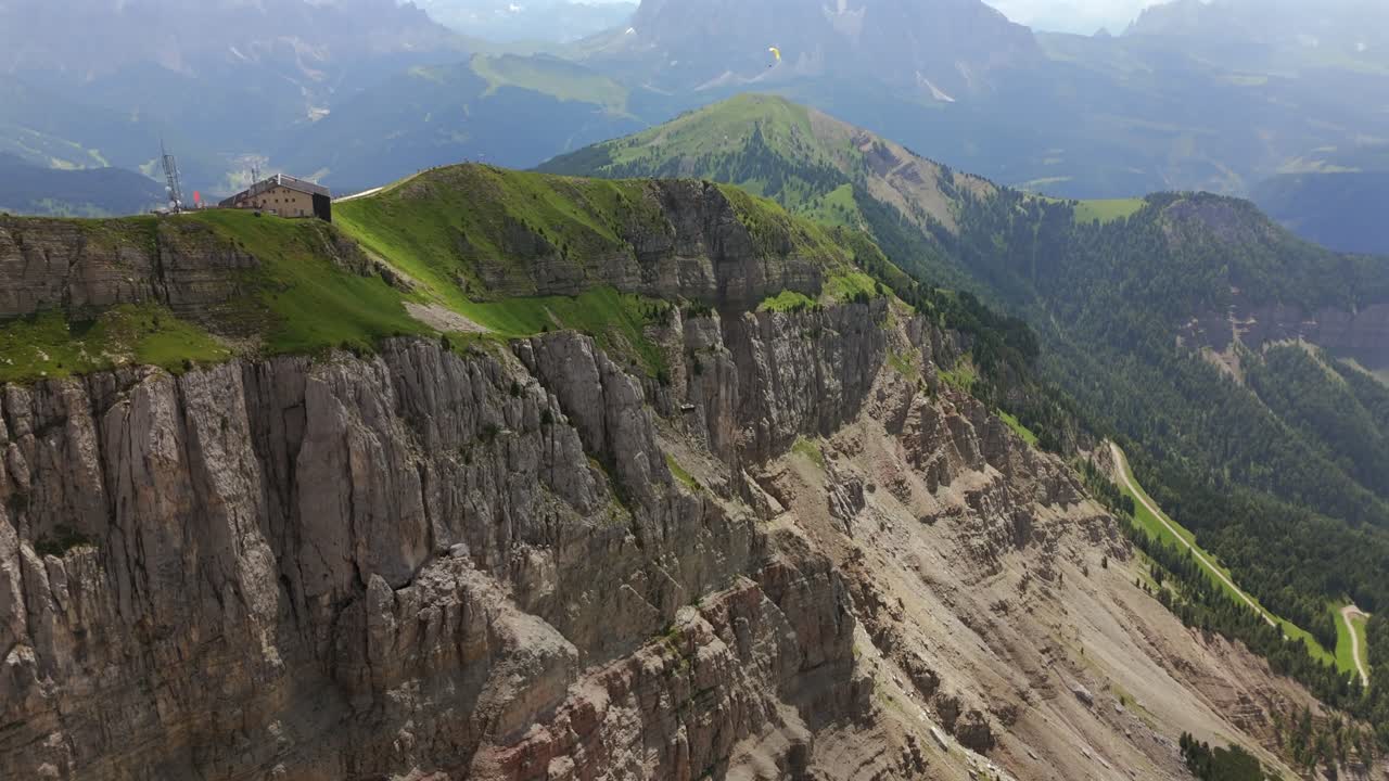 impresionantes imágenes aéreas de una remota cabaña de montaña situada en el borde de un acantilado rocoso en las dolomitas, italia, rodeada de exuberantes colinas verdes