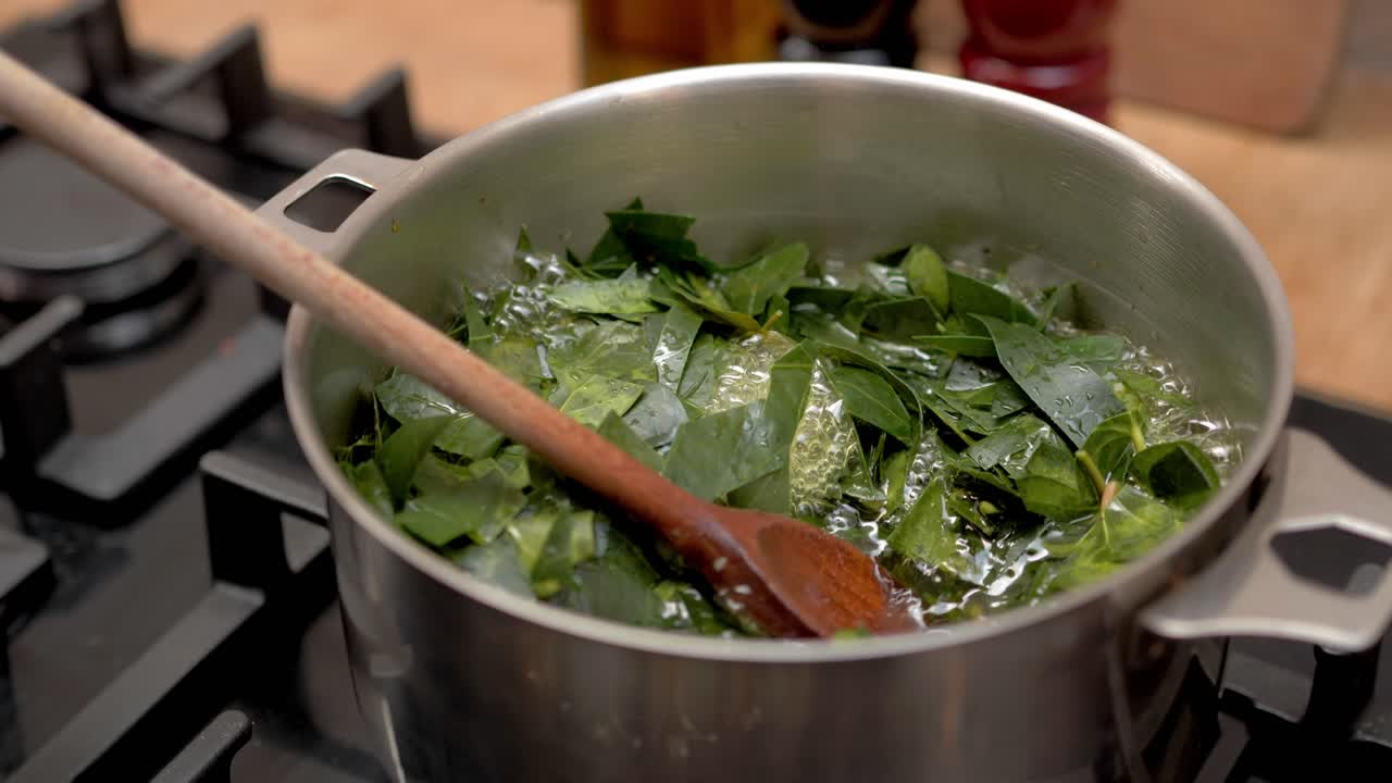 Foglie di edera che bollono in una pentola di metallo su un fornello a gas. Preparazione di detersivo naturale fatto in casa per il bucato dalle piante. Foglie verdi che cuociono in acqua calda con un cucchiaio di legno.
