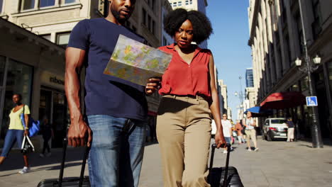 a couple navigating a city street with luggage and a map