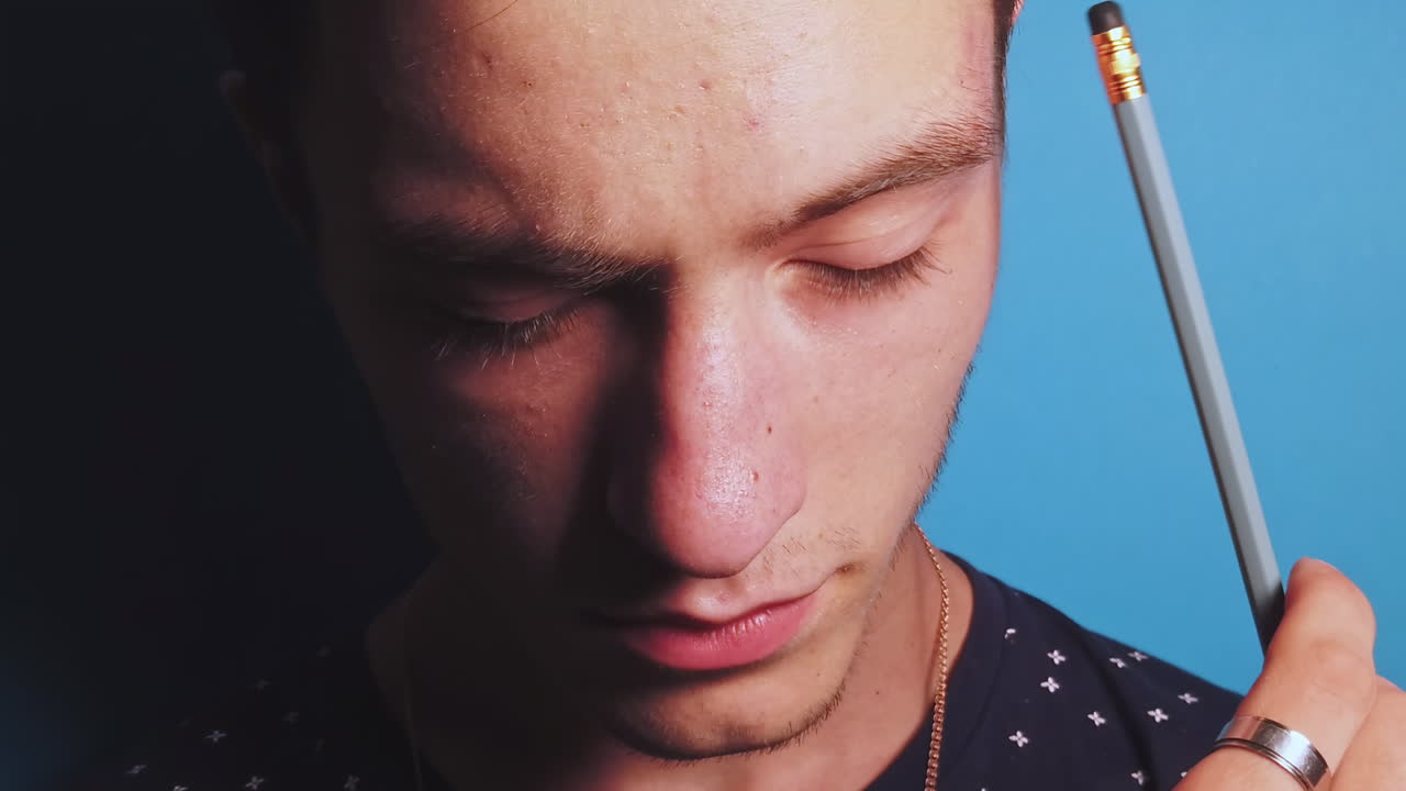 Close-up slow motion of thinking man with a pencil in front of a blue background