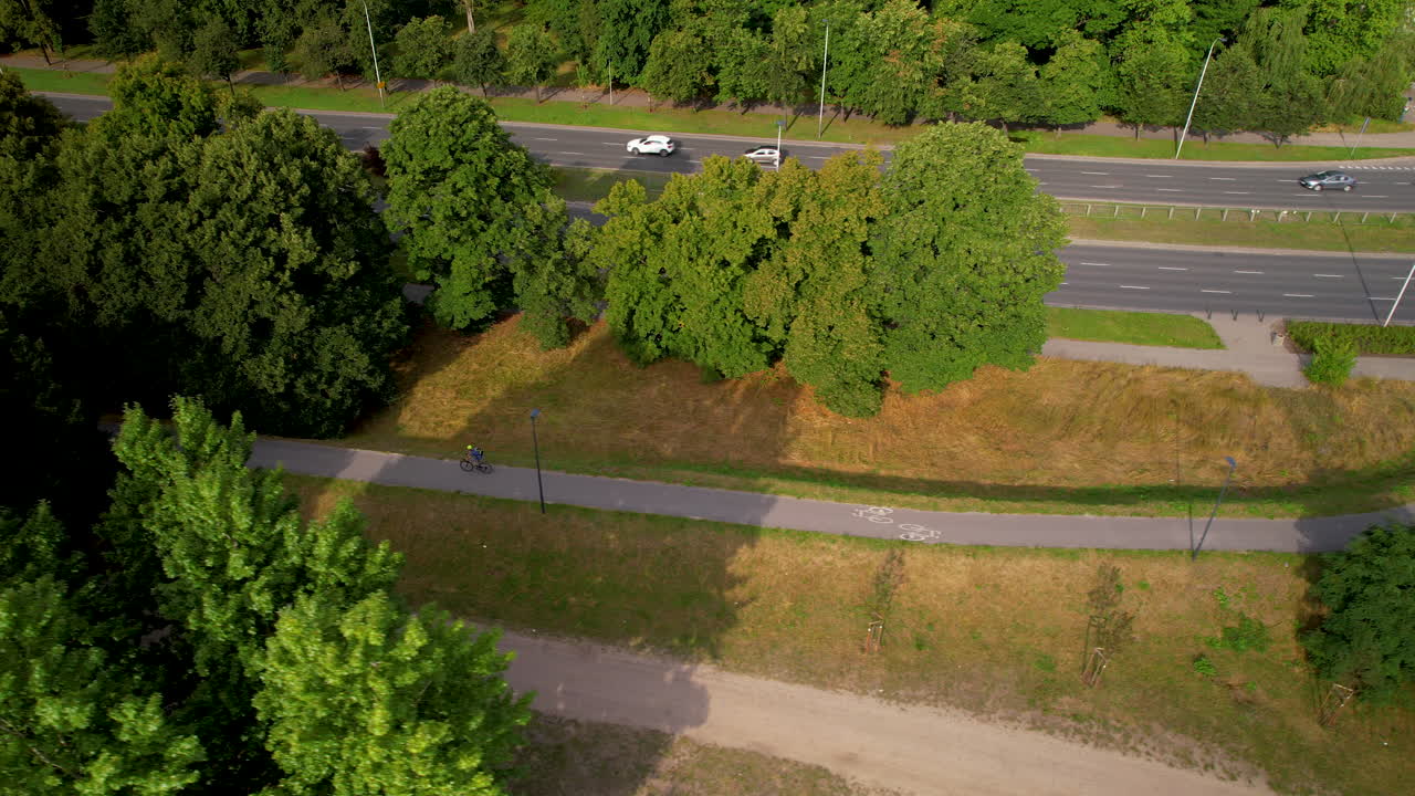 ciclista en bicicleta por el camino de la bicicleta a través del parque verde por la autopista wioslarska en varsovia - seguimiento aéreo