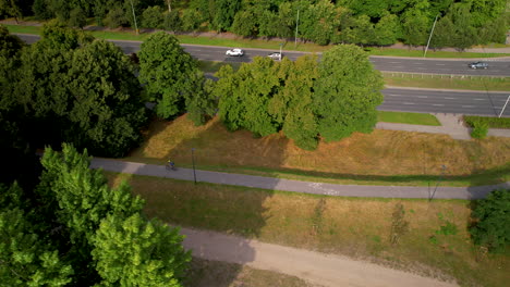 Ciclista-En-Bicicleta-Por-La-Carretera-A-Través-Del-Parque-Verde-Por-La-Autopista-Wioslarska-En-Varsovia---Seguimiento-Aéreo