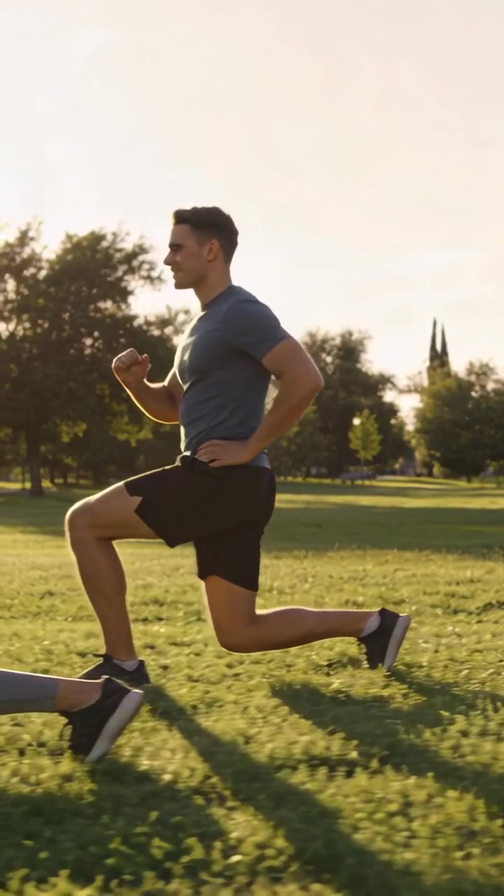 Vertikal video: Løbende fit mand springer over parkplæne, kammerat starter øvelse, i shorts og sko.
