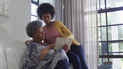 african american mother and adult daughter sitting on the couch and using tablet