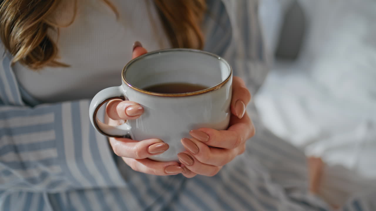 Woman hands holding coffee mug in bedroom closeup. Unrecognizable girl with cup