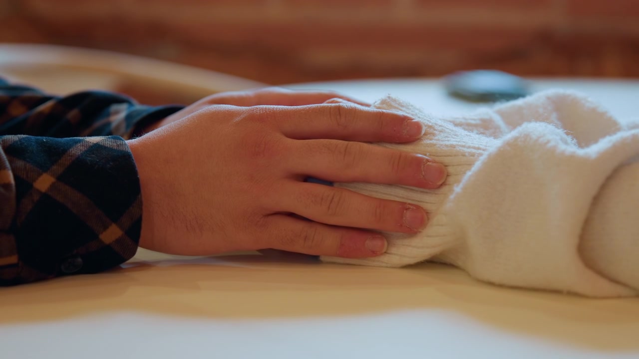Primo piano delle mani di una persona che puliscono delicatamente un tessuto bianco su un tavolo di legno. Il soggetto indossa abiti a quadri e usa movimenti delle mani delicati e intenzionali per pulire il materiale in un ambiente interno con illuminazione calda.